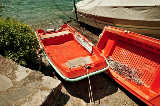 An empty orange boat sits by the water.