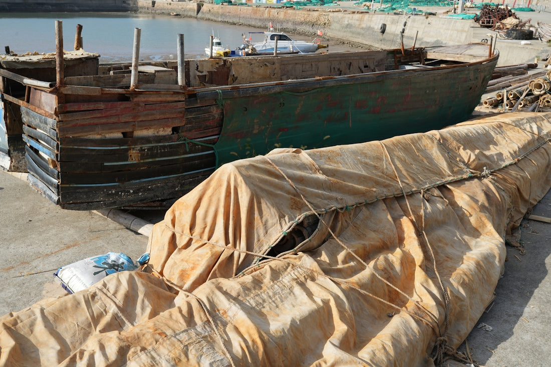 Wooden boat hull covered with tarp on shore
